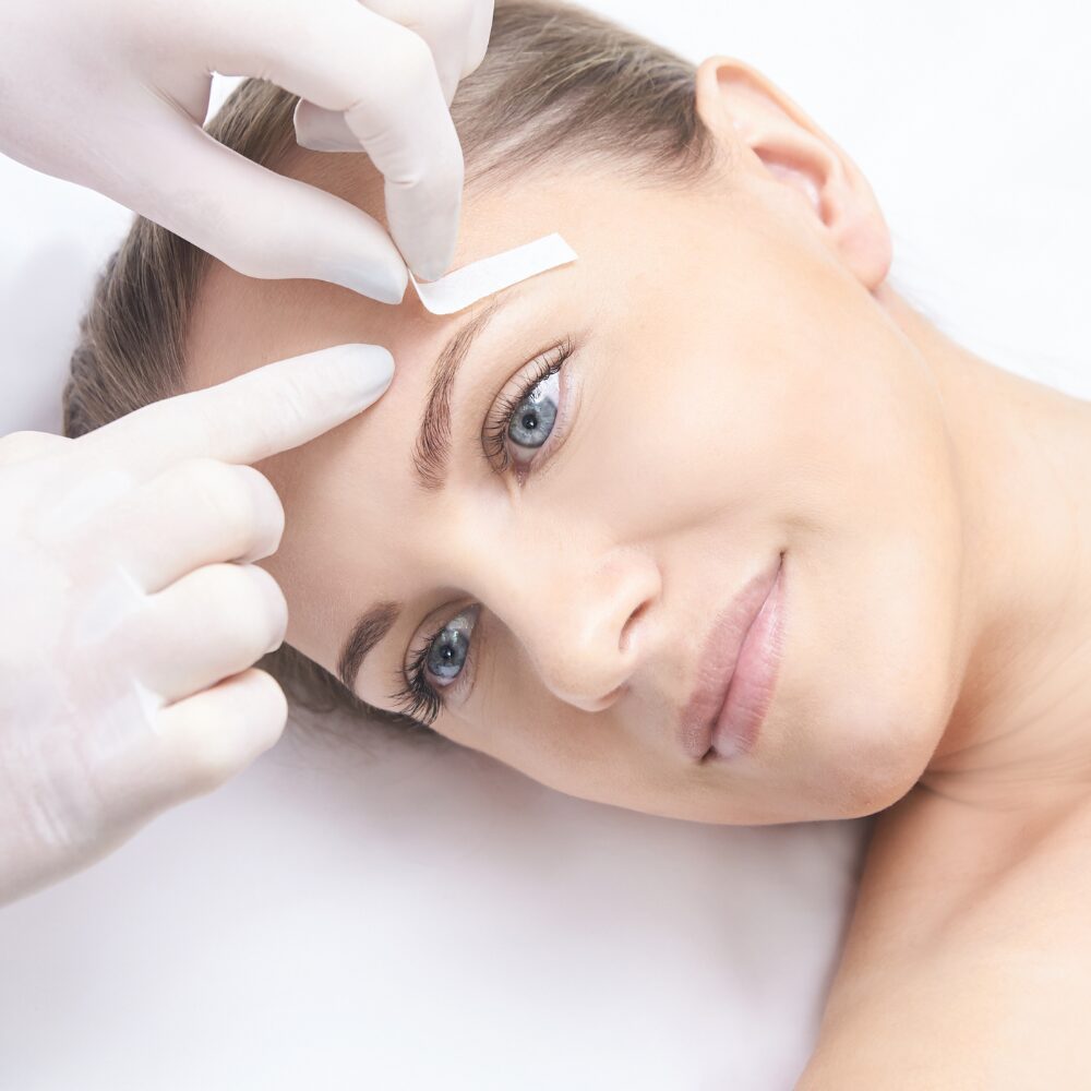 Woman receiving cosmetic treatment on her face with gloves on a white background