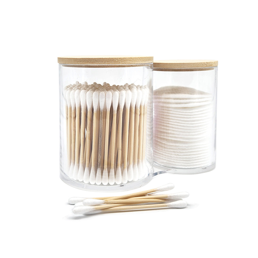 Two glass containers with wooden lids, one holding cotton swabs and the other cotton pads, on a white background.