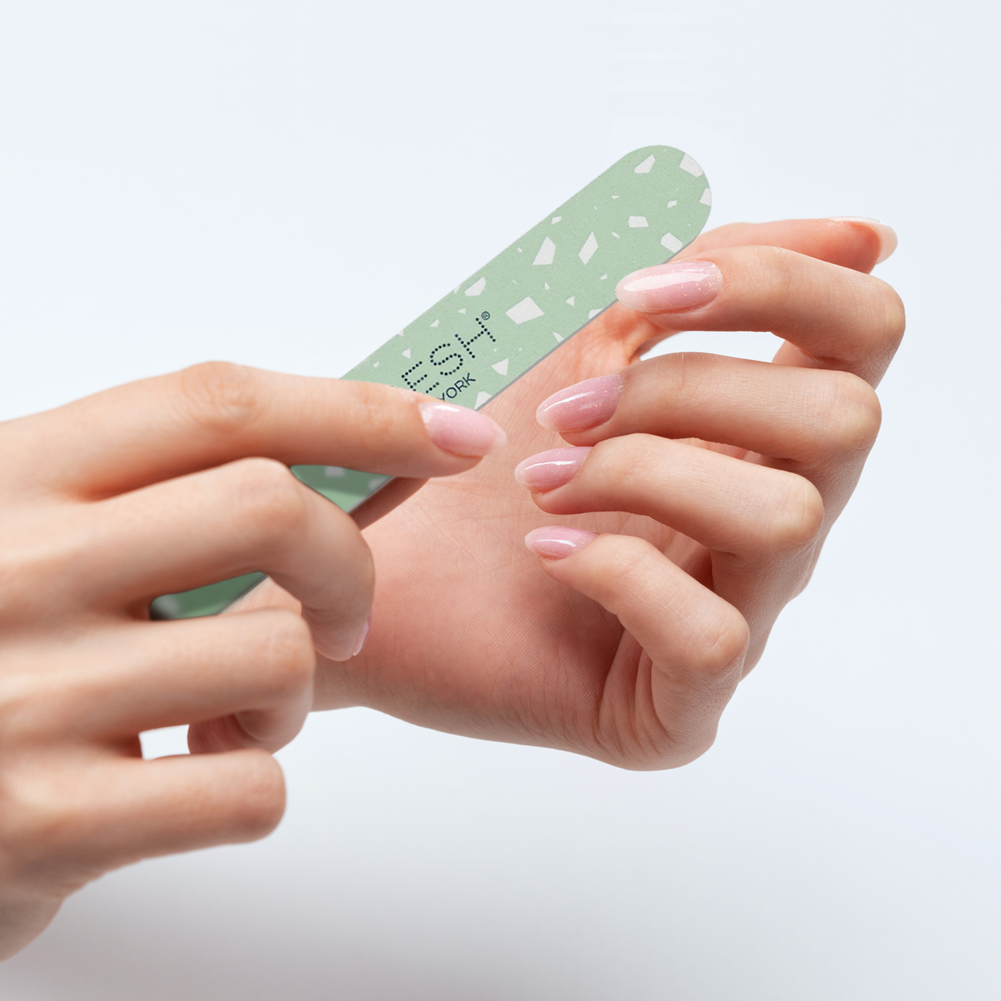 Hand using a green nail file on a light gray background