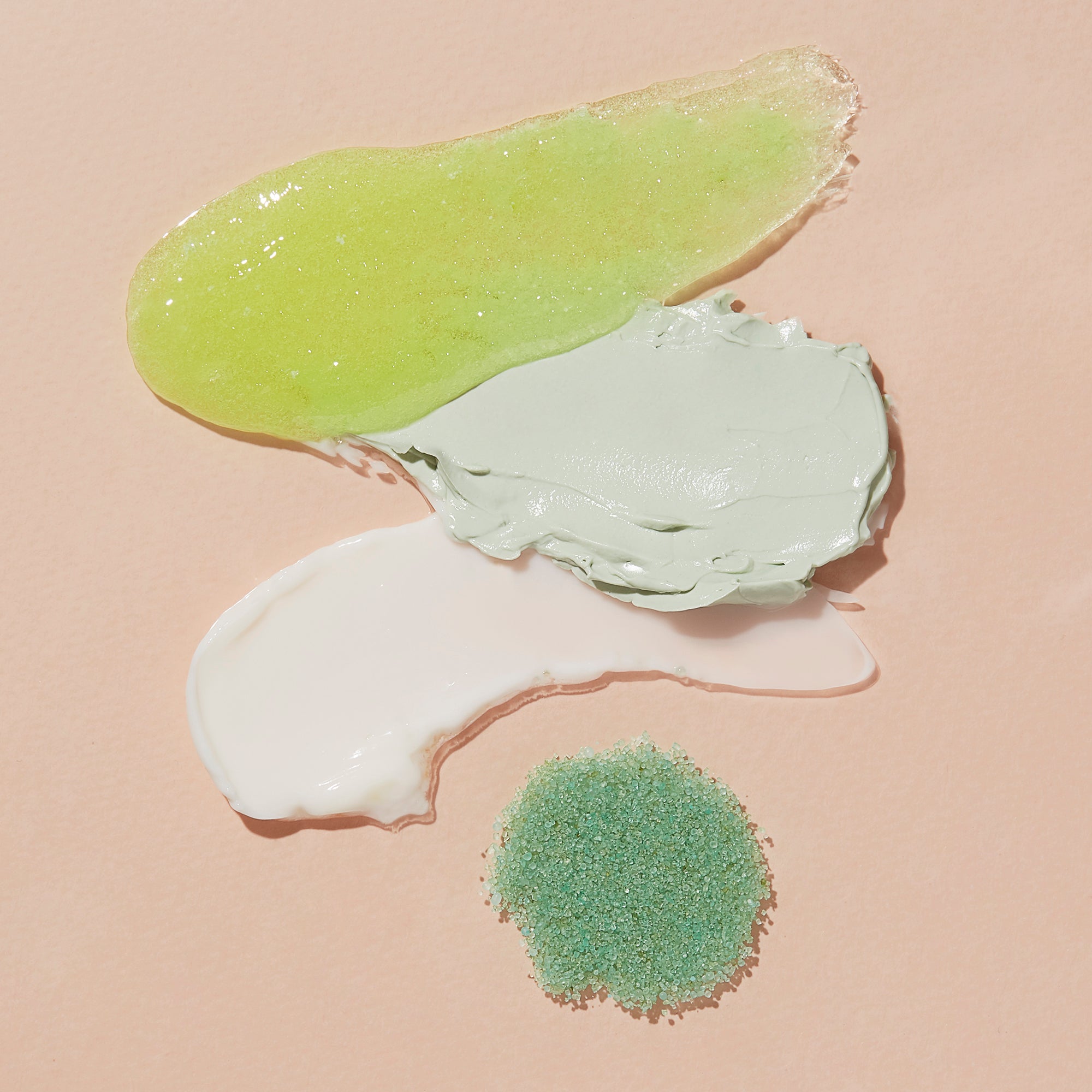 Three different textures of green cream on a beige background