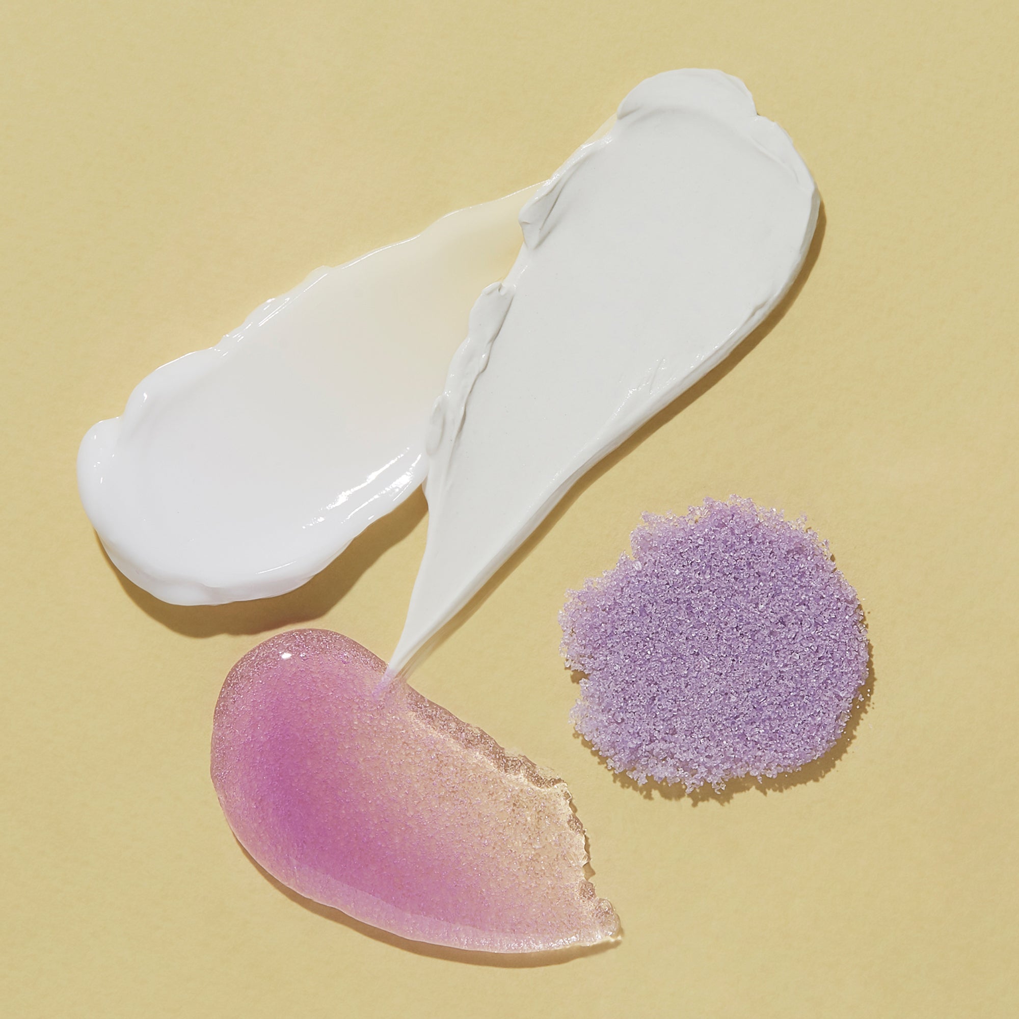 Three cosmetic products on a beige background: a white cream, a pink cream, and a purple sponge applicator.